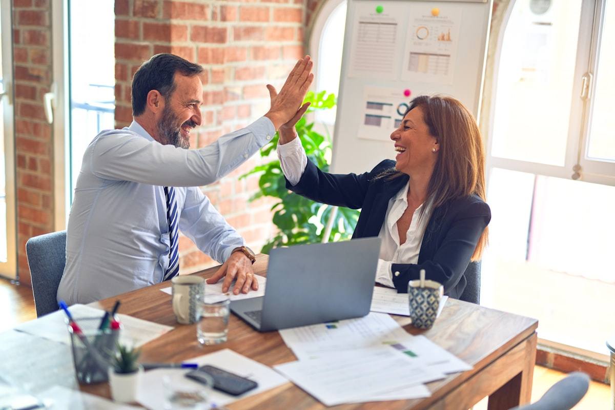 Two colleagues celebrating with a high five at an office desk