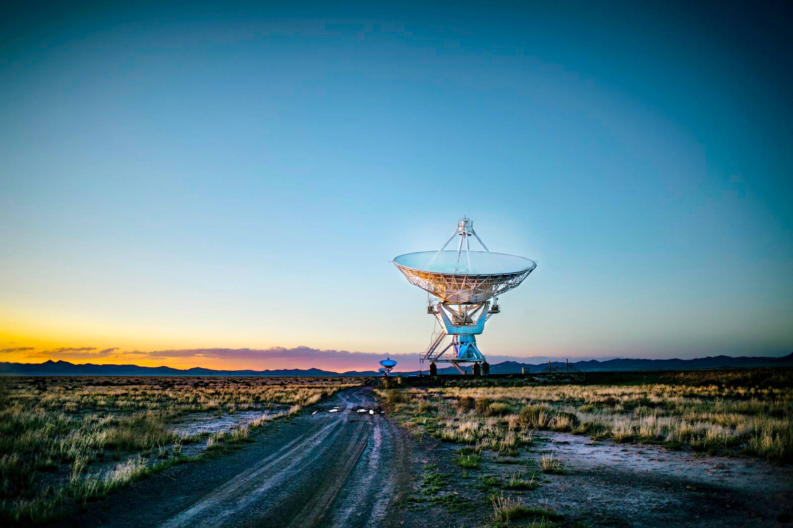 Large radar antenna dish in an open field at dusk